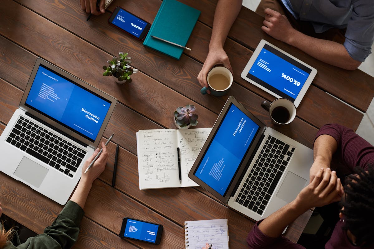A bunch of people working at a table with a bunch of laptops