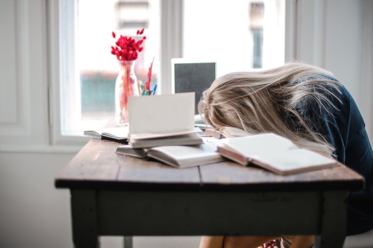 A person resting their head on a desk with books on it