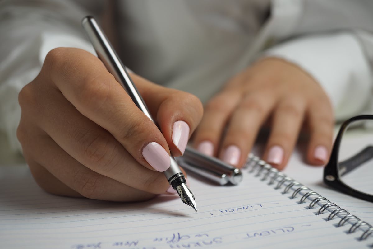 Person with painted nails writing in a notebook