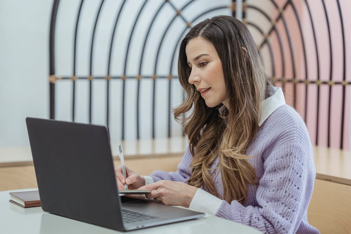 A lady writing something down in front of a laptop