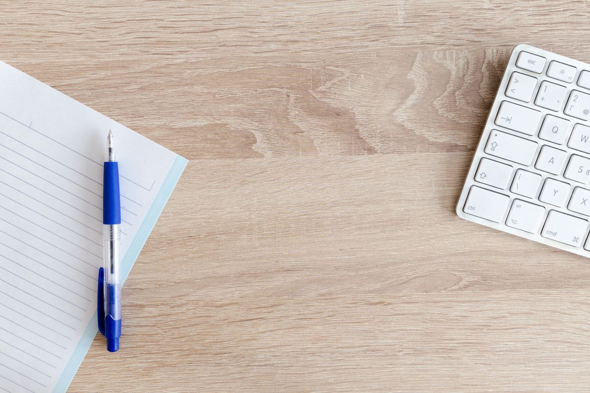 A pen on a notebook next to a white keyboard
