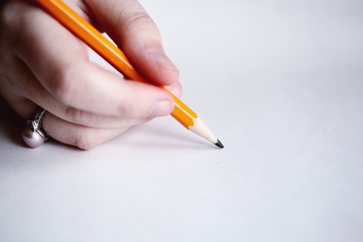 A person holding a pencil to a piece of paper